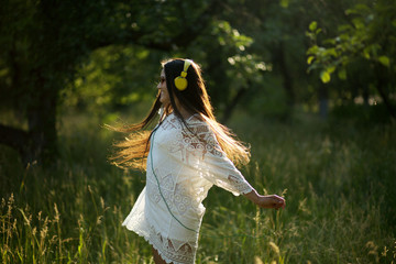 Happy young girl dancing with headphones on. Joyful lady in pretty white dress spins around in...
