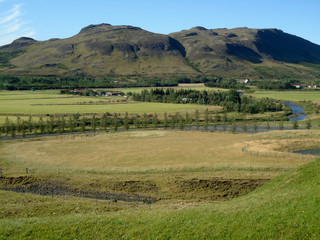Obraz premium Landscape in Iceland countryside. Mountains, river, meadow and a small town. 