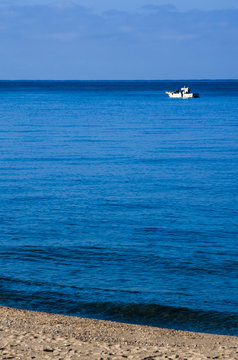 fishing boat sailing alone in the blue sea near the beach on a sunny day