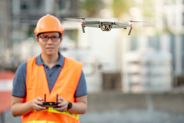 Young Asian engineer flying drone over construction site. Using unmanned aerial vehicle (UAV) for land and building site survey in civil engineering project.