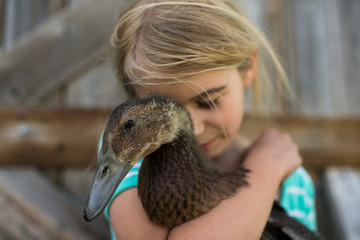 Girl with eyes closed hugging farm duck