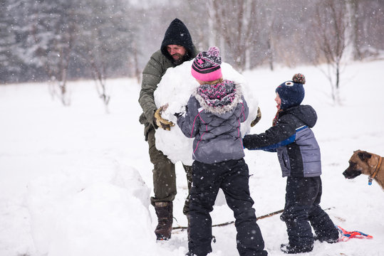 Father and children carrying large snowball