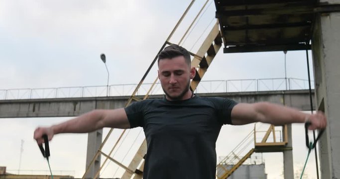 Workout exercise. Portrait of healthy handsome active man with fit muscular body doing expander stretching exercises outdoor. Sporty male training outdoor. Sports and fitness concept