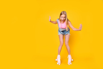 Fototapeta na wymiar Portrait of shocked wondered girl learning roller skating keeping balance trying not to fall down isolated on yellow background, wellness activity workout fitness concept