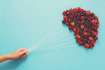 Hand holding balloons made of berries on blue paper background. Healthy eating concept. Flat lay....