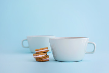 Two big cups of coffee and sandwich cookies on blue background.
