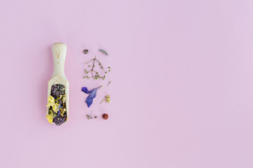 Dried flowers in wooden spoon on pink background. Flat lay, top view.