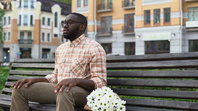Nervous young man waiting for girl, sitting park bench with flowers, blind date