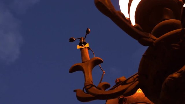 Wind vane, weather vane mounted under the streetlamp.
Revolving pointer showing the direction of the wind.
Night scene, sunset, blue sky, clouds moving in the background. Forecast concept. Low angle