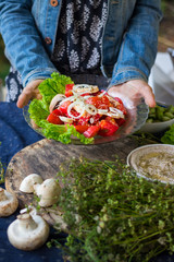 Woman hands holds vegetables salad with ripe red tomatoes and onion rings on big green salad leaves. Served with Israeli chickpea hummus spread with sesame seeds tahini. Raw vegan vegetarian food