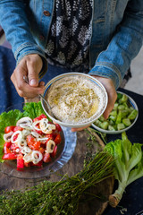 Woman hand adds homemade tahini paste. Traditional Arabic, Istraeli food - white sesame seeds paste used for lunch or dinner with vegetables as main sauce or dip. Raw vegan vegetarian healthy food