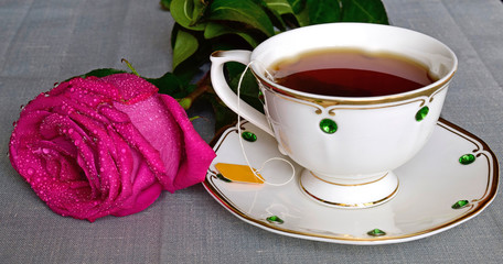On the table lay a rose, standing next to a porcelain Cup with tea.
