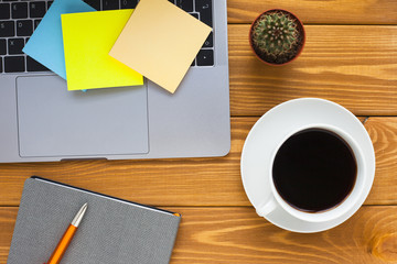 Laptop, white cup of coffee, cactus, snacks and notebook on the bright wooden background. Business, office, education, planning concept. Top view. Close up.