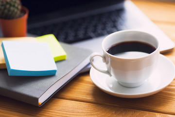 Laptop, white cup of coffee, cactus, snacks and notebook on the bright wooden background. Business, office, education, planning concept. Top view. Close up.