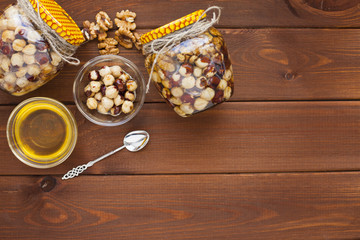 Natural honey and nuts in glass jars, vintage silver spoon on the wooden background. Healthy food, diet, lifestyle concept. Top view. Close up.
