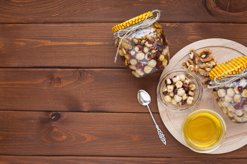Natural honey and nuts in glass jars, vintage silver spoon on the wooden background. Healthy food, diet, lifestyle concept. Top view. Close up.