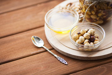Natural honey and nuts in glass jars, vintage silver spoon on the wooden background. Healthy food, diet, lifestyle concept. Top view. Close up.