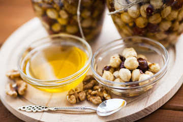 Natural honey and nuts in glass jars, vintage silver spoon on the wooden background. Healthy food, diet, lifestyle concept. Top view. Close up.