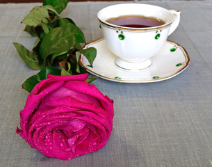 On the table lay a rose, standing next to a porcelain Cup with tea.