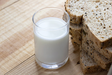 A glass of milk and bread placed on the wood table.