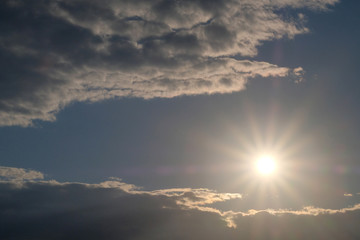 Beautiful sun with rays of light on a background of clouds. Evening or morning sky.