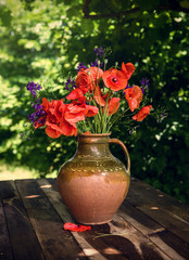 Clay vase with flowering poppies on a wooden table. Traditional Ukrainian bouquet.
