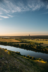 Beautiful nature landscape at sunset time. View from mountain to green meadows and fields with river and nuclear power plant far away. Summer travel tranquil background