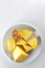 Pieces of pineapple on a white plate, pineapple on a white background top view, salad of tropical fruits for breakfast, vegetarian food, copy space