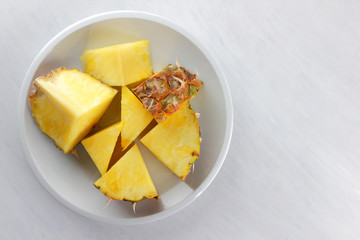 Pieces of pineapple on a white plate, pineapple on a white background top view, salad of tropical fruits for breakfast, vegetarian food, copy space