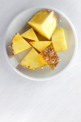 Pieces of pineapple on a white plate, pineapple on a white background top view, salad of tropical fruits for breakfast, vegetarian food, copy space