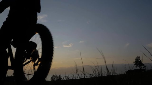 Fat bike also called fatbike or fat-tire bike in summer riding in the grass. The athlete passes in a frame silhouette against a beautiful sunset on the sea. Everything happens in deep grass.