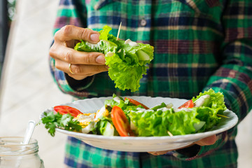 Woman hands holds vegan spring rolls. Cucumbers wrapped in salad leaves with tomatoes, vegan mustard sauce and homemade sesame seeds tahini paste. Vegetarian healthy food.