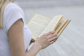 Naklejka premium Young female hand holding an old book - reading outdoors
