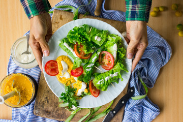 Woman hands holds vegan spring rolls. Cucumbers wrapped in salad leaves with tomatoes, vegan mustard sauce and homemade sesame seeds tahini paste. Vegetarian healthy food.