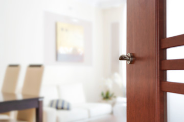 Blurred view through opened wooden door to a modern living room or apartment interior (copy space).