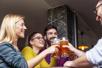 Group of four people toasting with glasses full of beer in local pub