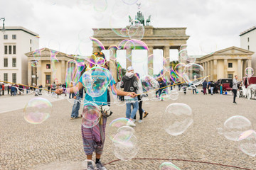 Street performer, busker, entertaining the crowd in front of the Brandenburg Gate in Berlin on an overcast summer day. Colorful soap bubbles floating in the foreground. © studiolaska