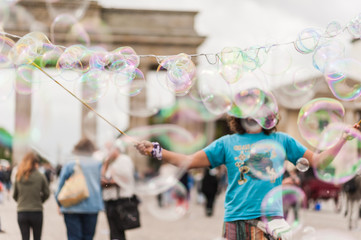 Street performer, busker, entertaining the crowd in front of the Brandenburg Gate in Berlin on an overcast summer day. Colorful soap bubbles floating in the foreground. © studiolaska
