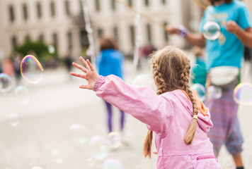 Street performer, busker, entertaining the crowd in front of the Brandenburg Gate in Berlin on an overcast summer day. Children playing with colorful soap bubbles floating in the foreground.