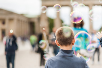 Street performer, busker, entertaining the crowd in front of the Brandenburg Gate in Berlin on an overcast summer day. Children playing with colorful soap bubbles floating in the foreground.