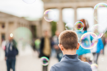 Street performer, busker, entertaining the crowd in front of the Brandenburg Gate in Berlin on an overcast summer day. Children playing with colorful soap bubbles floating in the foreground.