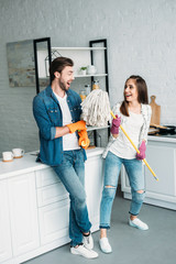 couple in rubber gloves having fun with mop in kitchen and pretending singing