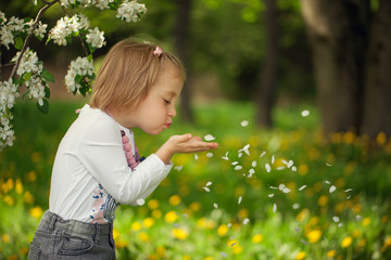 Girl blowing flower petals in the park on a summer.