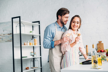 Fototapeta premium boyfriend hugging girlfriend and they holding glasses on wine in kitchen