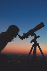 Young woman looking at the sky with astronomical telescope.