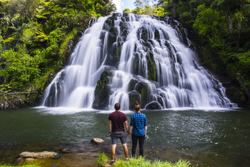 Travel New Zealand. Young tourist couple/friends overlooking waterfall. Popular tourist attraction in North Island. Long exposure falling water. Summer holidays. Natural, outdoor, travel background.