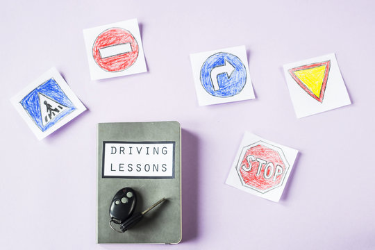 Training notebook for driving lessons and driving traffic rules next to the road sign drawings to get a driving license. On a purple background next to the car keys