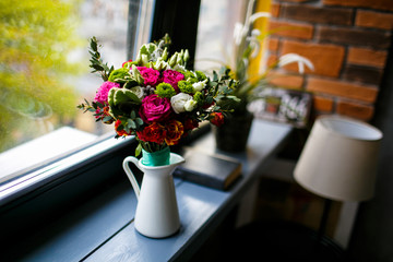 White jar of pink and white roses on a wooden windowsill