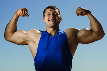 the athlete on the beach posing on blue sky background. Strong hands