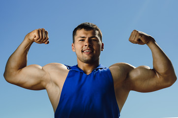 the athlete on the beach posing on blue sky background. Strong hands